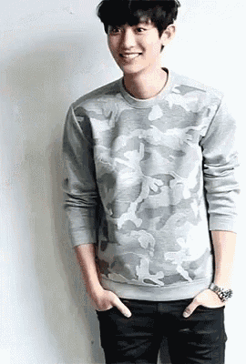 a young man wearing a grey camouflage sweater and black jeans is smiling .