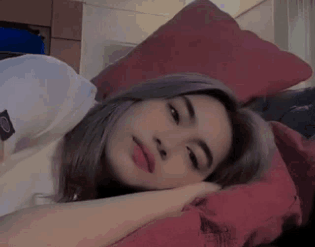 a woman is smiling while laying on a bed with a red pillow .