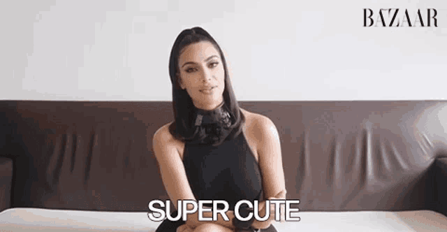 a woman in a black dress is sitting on a couch and says `` super cute '' .