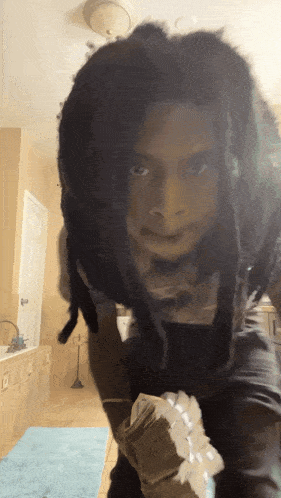 a person with dreadlocks is standing in a bathroom with a blue rug