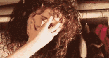 a woman with curly hair is covering her face with her hand while laying on a bed .