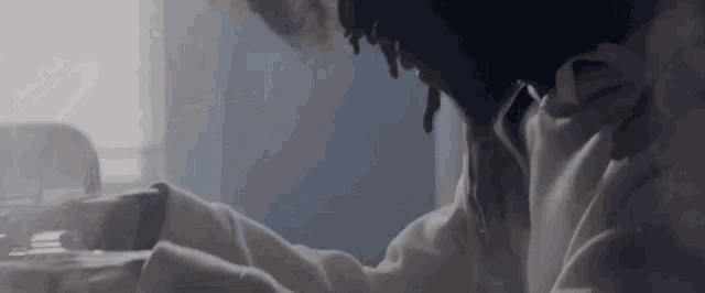 a man in a white shirt is sitting in front of a window with his head down .