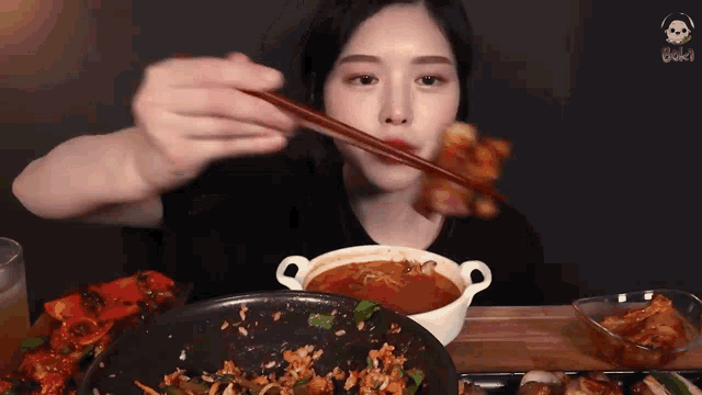 a woman is eating food with chopsticks from a bowl of soup .