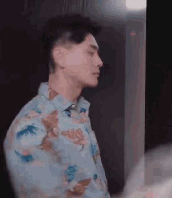 a man in a hawaiian shirt is standing in a room and looking at something .