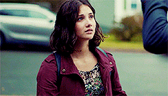 a woman wearing a purple jacket and a floral shirt is sitting on the sidewalk .
