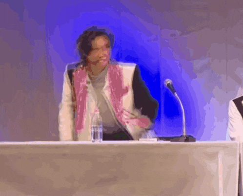 a woman in a pink jacket is standing at a podium with a microphone