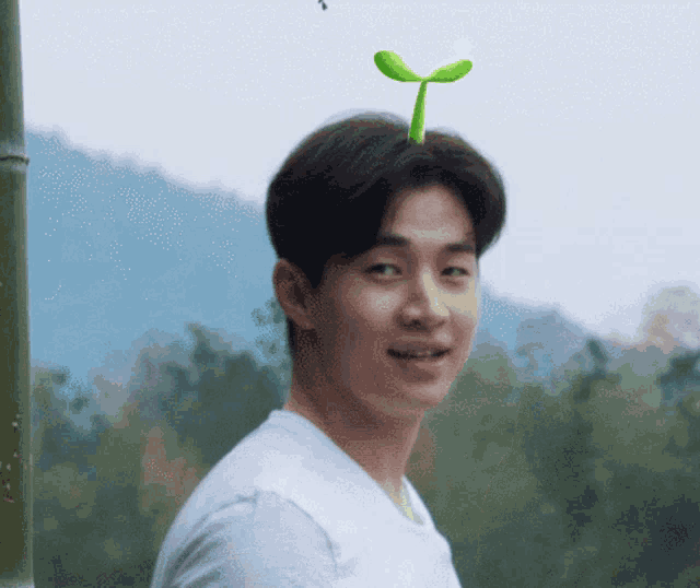 a man with a plant on his head looks at the camera