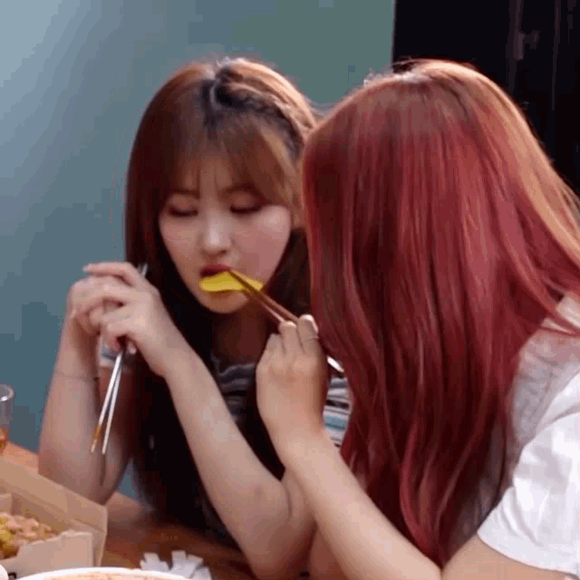 two girls with red hair are sitting at a table eating with chopsticks