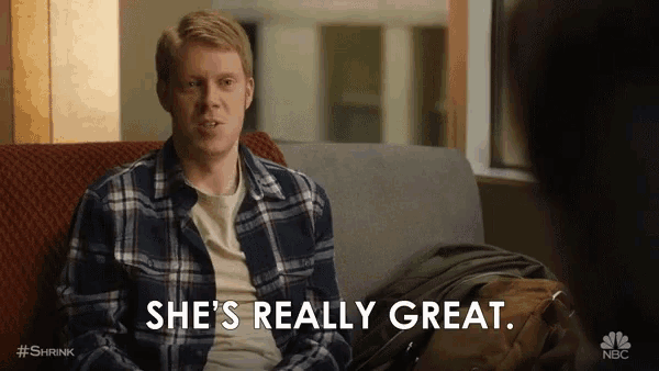 a man in a plaid shirt is sitting on a couch and says she 's really great
