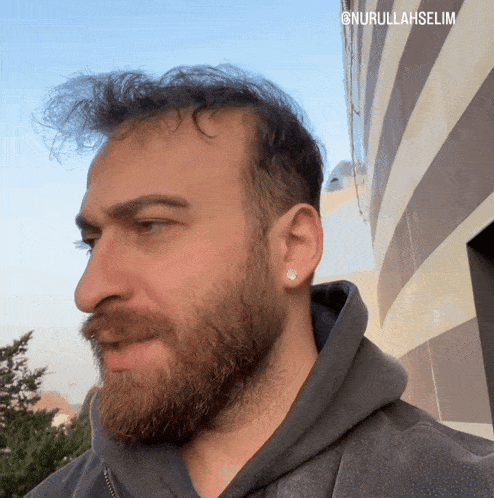a man with a beard is wearing a gray hoodie and earring