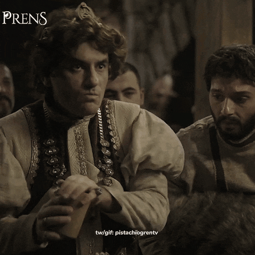 a man with a crown on his head sits in front of a sign that says " prens "