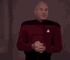 a man in a red shirt is standing in front of a wall and says well if you will excuse me