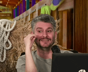 a man sitting in front of a laptop with a ranch sign behind him