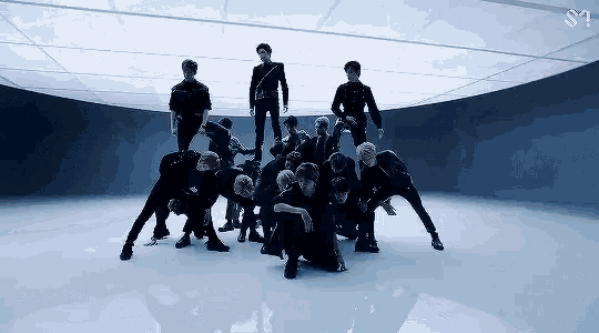 a group of young men are dancing in a dark room with a sm logo in the corner