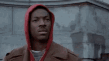 a man wearing a red hooded jacket is standing in front of a building .