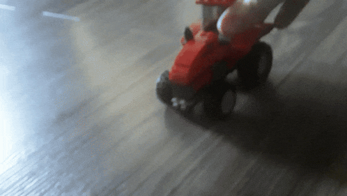 a red toy tractor is driving down a wooden road