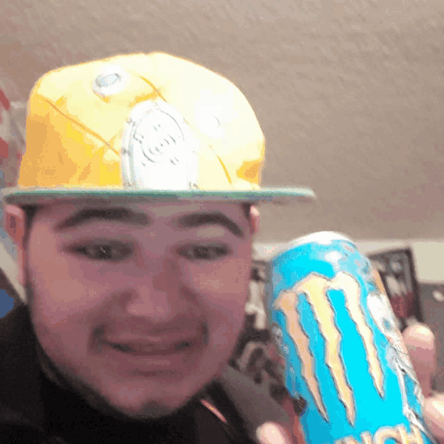 a man wearing a yellow hat is holding a monster energy drink
