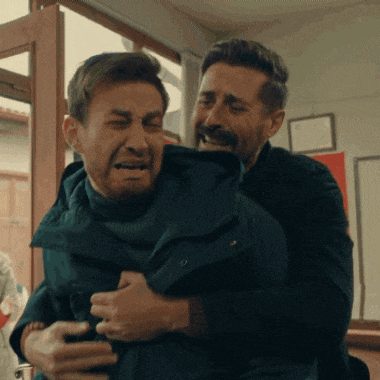 a man is holding another man in his arms who is crying