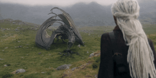a woman with dreadlocks stands in front of a fallen dragon