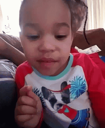a little girl is sitting on a couch wearing a red shirt with a raccoon on it .