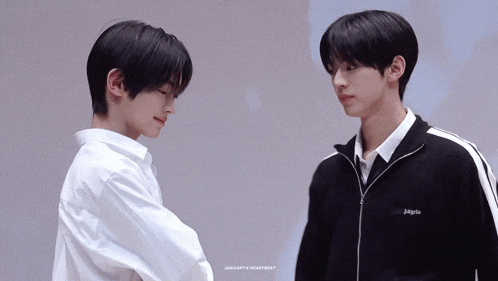 two young men are standing next to each other and one of them is wearing a white shirt and a black jacket .
