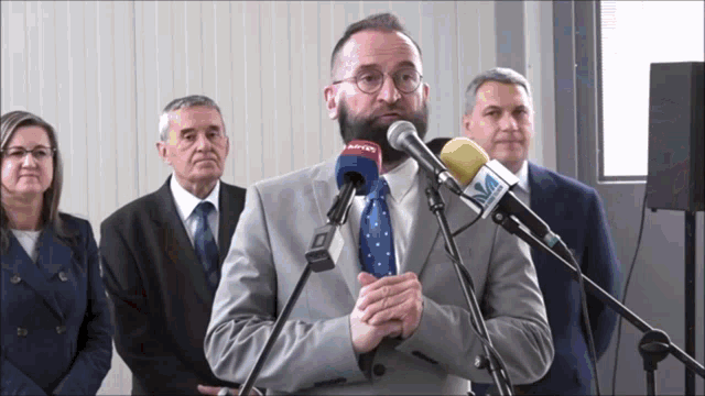 a man in a suit and tie stands in front of a microphone that says adntv on it