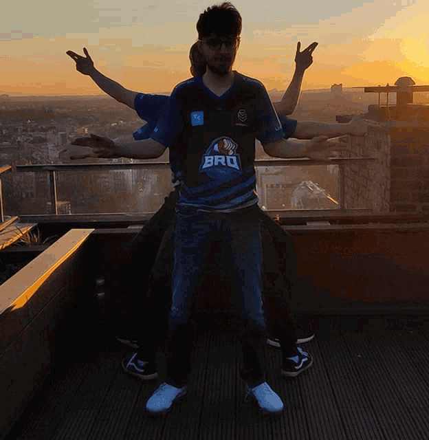 a man wearing a bro shirt stands on a balcony with his arms outstretched