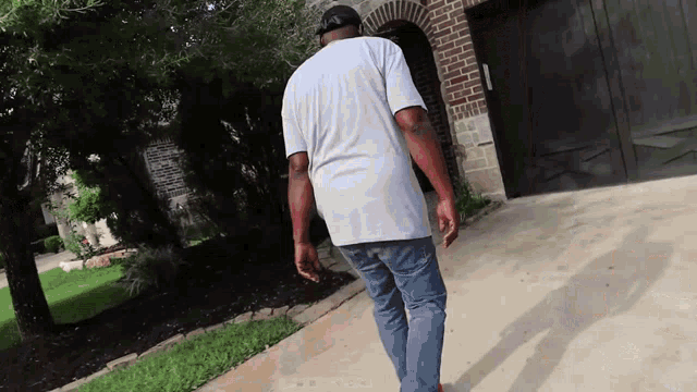 a man in a white shirt and blue jeans walks down a sidewalk