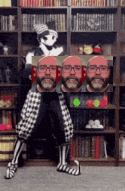 a man with glasses and a beard is sitting in front of a bookcase