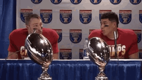two football players are sitting at a table in front of a liberty bowl banner