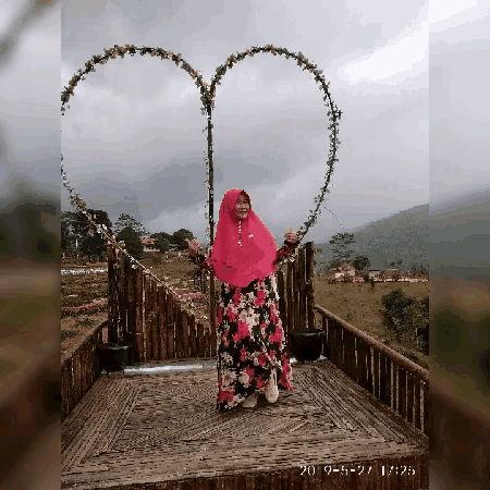 a woman in a pink hijab stands in front of a heart shaped swing