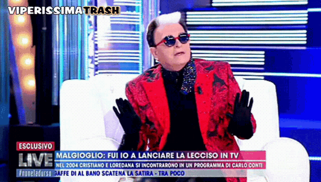 a man in a red suit and sunglasses is sitting on a couch in front of a screen that says viperissima trash