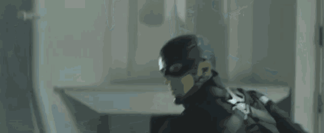 a man in a mask is standing in a room with people laying on the floor and a door in the background .