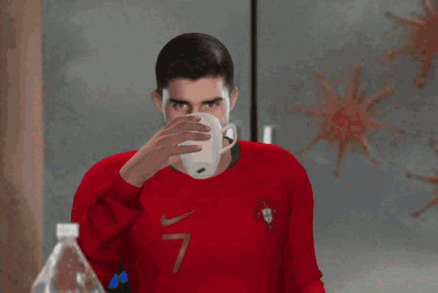 a man in a red nike shirt drinks from a glass next to a bottle of aquafina water