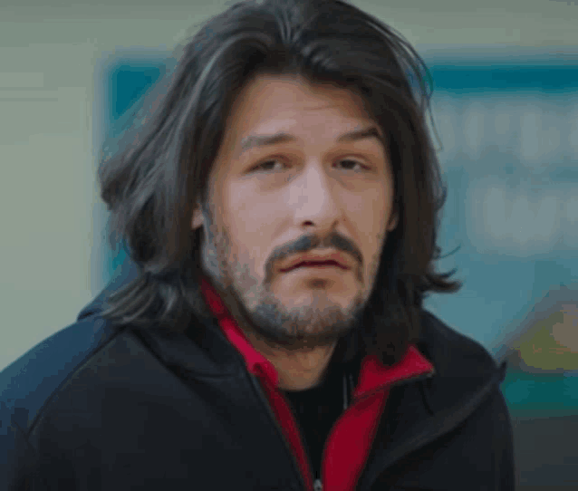 a man with long hair and a beard is wearing a red jacket