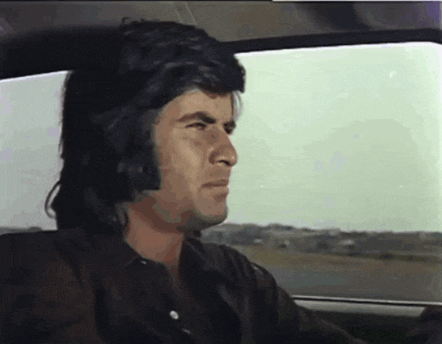 a man with long hair is sitting in a car and looking out the window