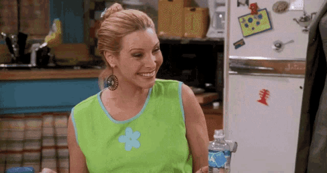 a woman in a green tank top is smiling in front of a refrigerator with a sticker on it