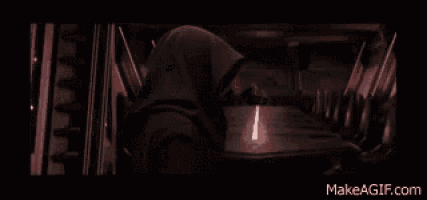 a man in a hooded robe is standing in a dark room with a red light coming out of his hand ..