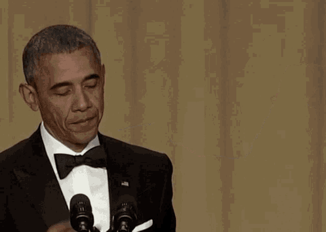 a man in a tuxedo and bow tie is giving a speech in front of two microphones
