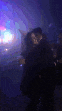 a man and a woman are dancing in a dark room with purple lights behind them .