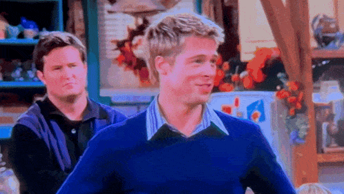 a man in a blue sweater is smiling while standing next to another man in a black shirt .