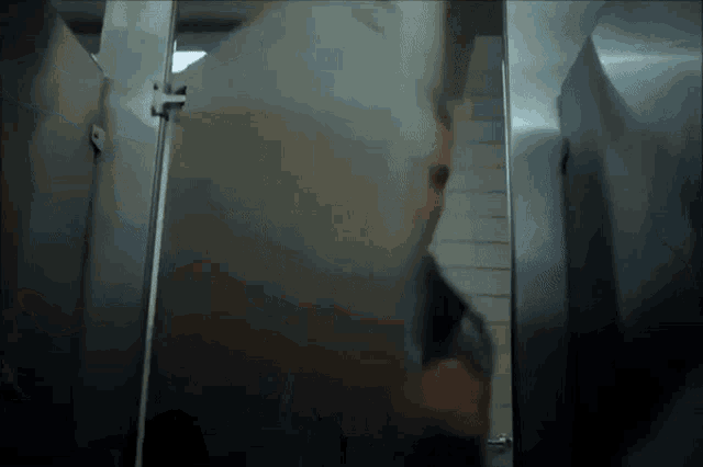 a man is standing in a public restroom behind a glass wall