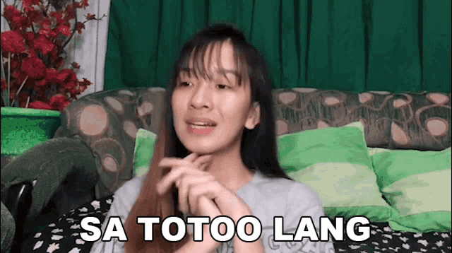 a woman is sitting on a couch with flowers in the background and says sa totoo lang