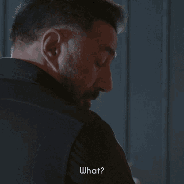 a man with a beard is looking over his shoulder and says " what "