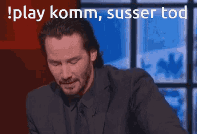 a man in a suit and tie is sitting in front of a sign that says ' play komm susser tod '