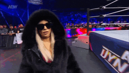 a woman in a fur coat and sunglasses walks into a wrestling ring that says dyn