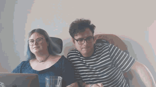 a man and a woman are sitting next to each other with the man wearing glasses and a striped shirt