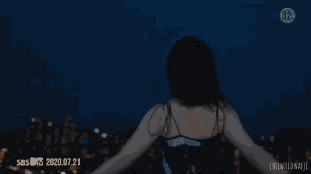 a woman in a blue dress is standing on top of a building at night .