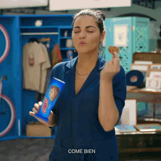 a woman in a blue jumpsuit holds a can of pringles chips
