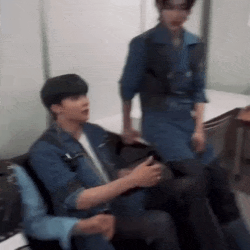 a blurry picture of a man sitting in a chair with another man standing behind him .